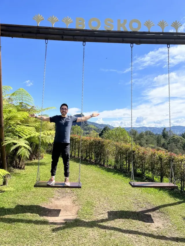 On the swings at Bosko in Guatapé, with El Peñol behind me, in May 2023